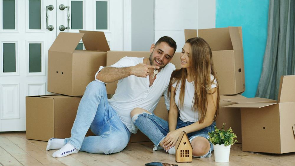 A couple laughing on the floor of their new home, among moving boxes
