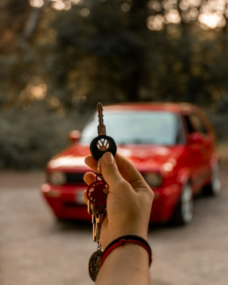 A hand holding up a car key in front of a red car